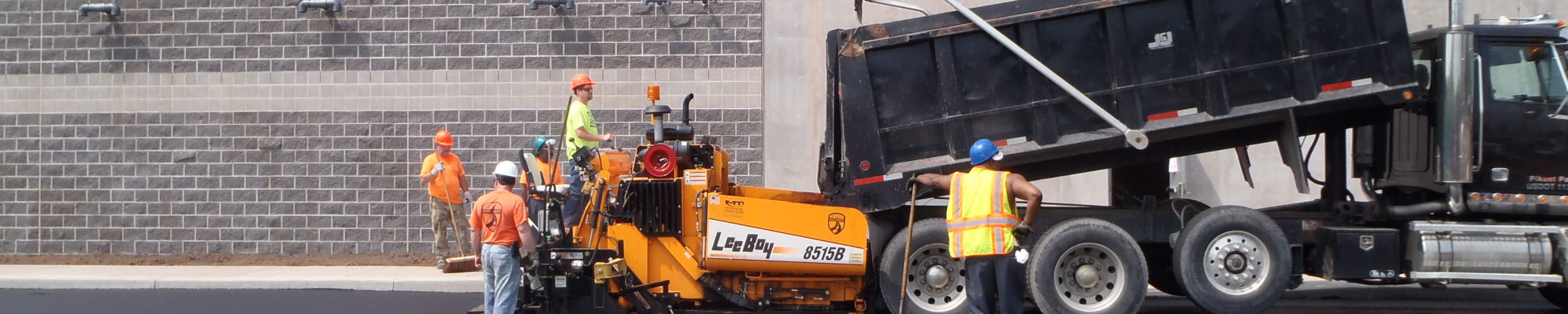 workers watching over truck dumbing pavement