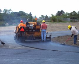 3 standing people smoothing pavement on a machine